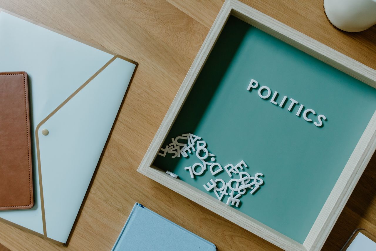 Top view of a box with POLITICS text alongside office items on a wooden desk.