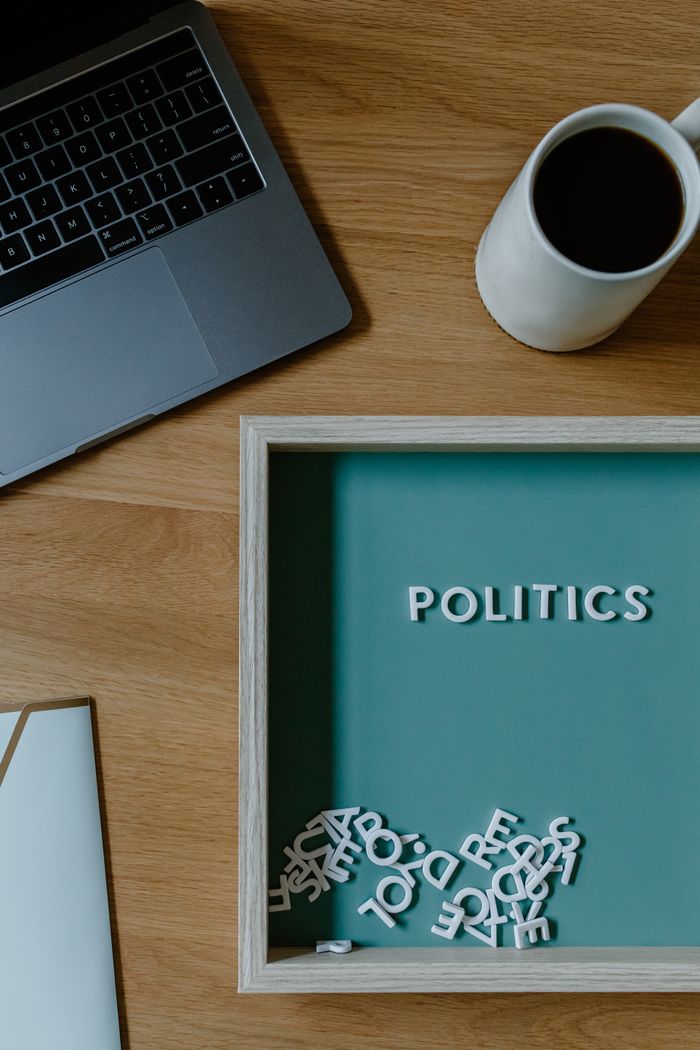 Top view of office desk with laptop, coffee, and letterboard displaying POLITICS.
