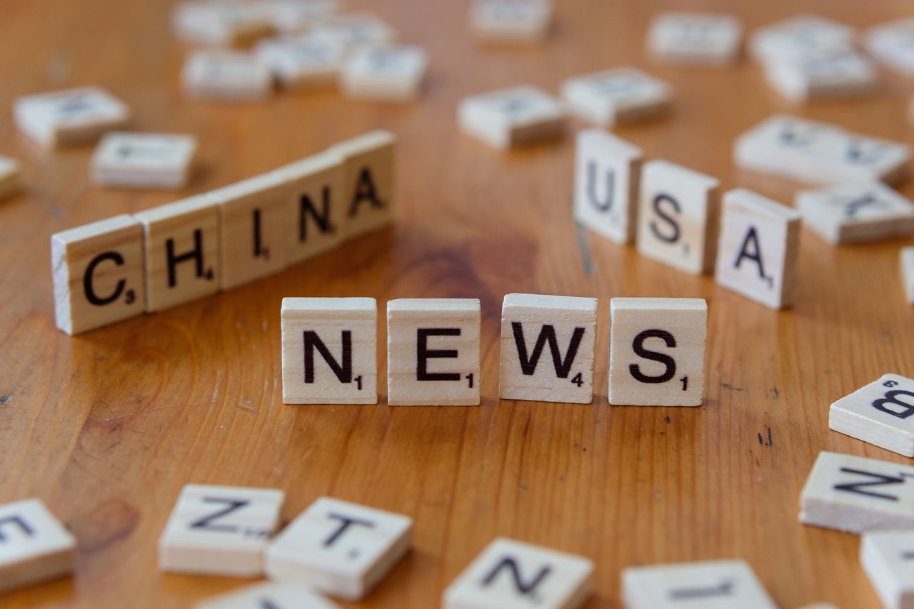 Wooden Scrabble tiles spelling NEWS with CHINA and USA on a wooden surface.