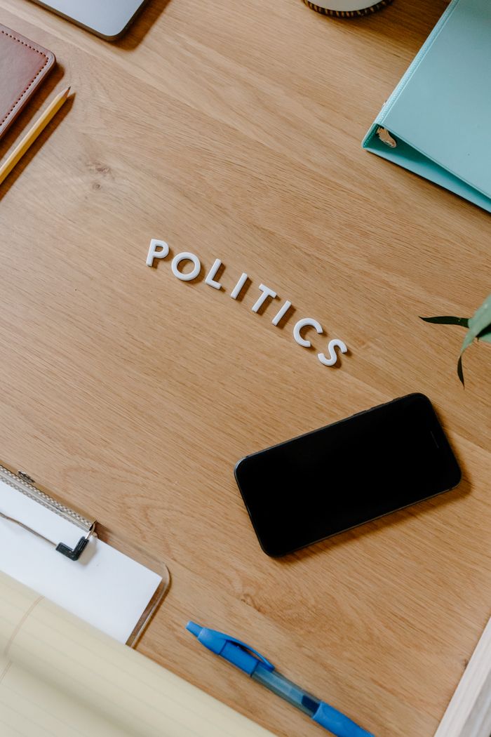 A modern office desk with a smartphone, notebooks, and politics spelled out, showcasing a conceptual theme.